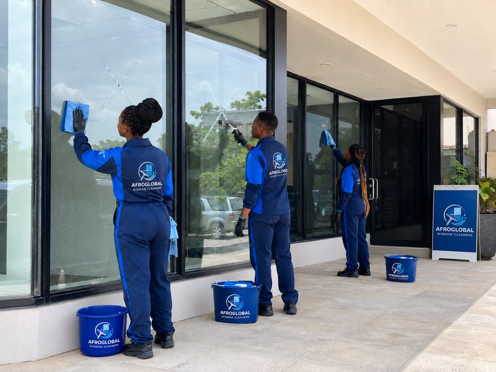 Cleaners removing builder's tape and residue from new commercial windows after construction